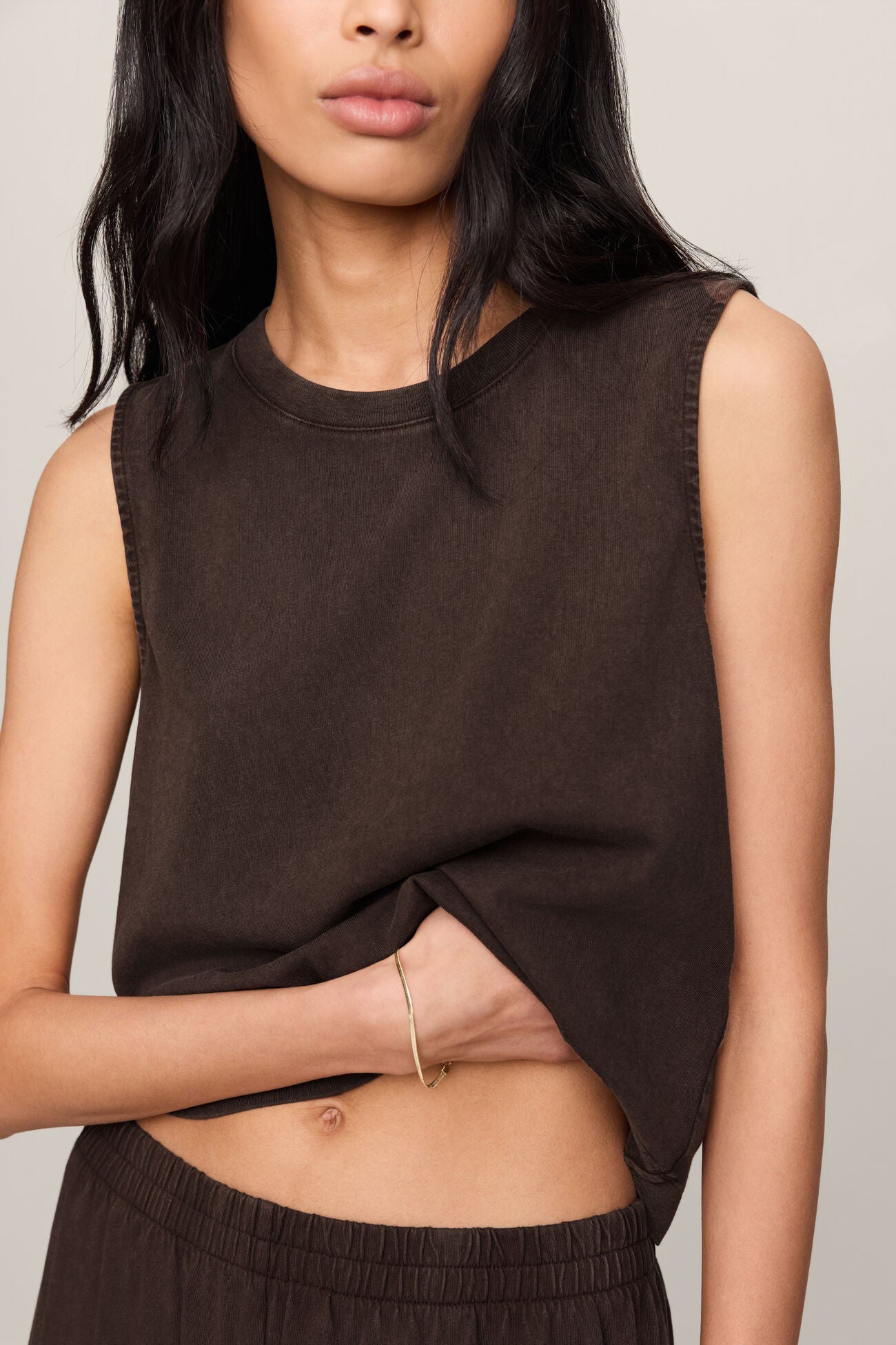 Woman wearing a brown sleeveless top and pants against a neutral background
