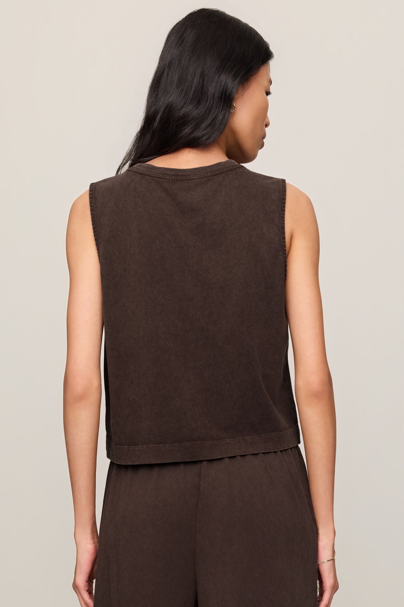 Woman wearing a brown sleeveless top and pants against a plain background