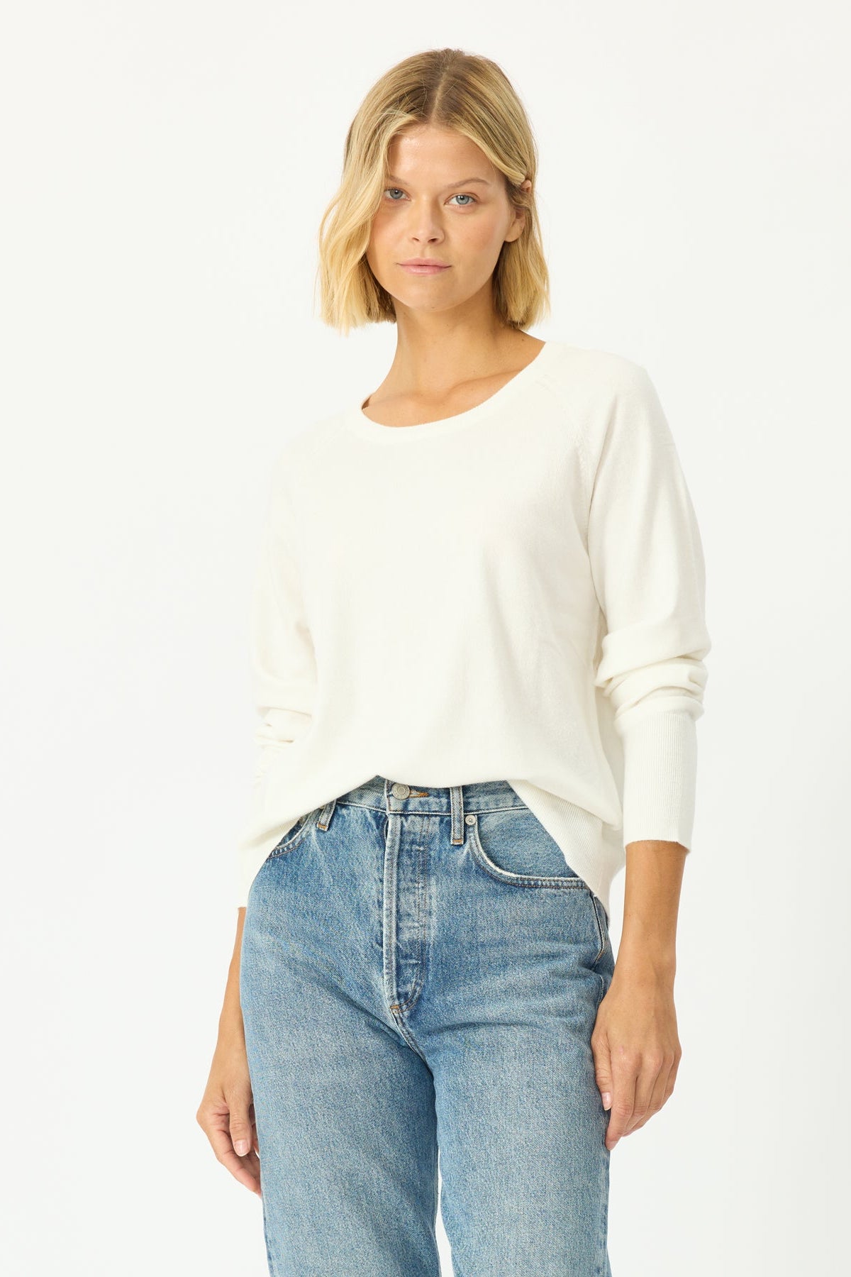 Woman wearing a white sweater and blue jeans on a white background