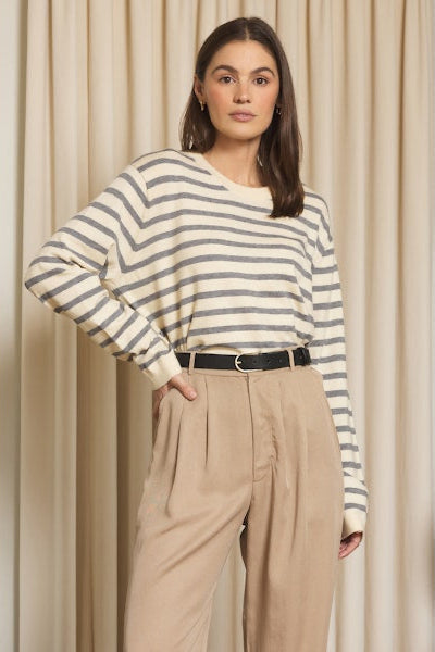 Woman wearing a striped sweater and beige pants against a beige curtain background