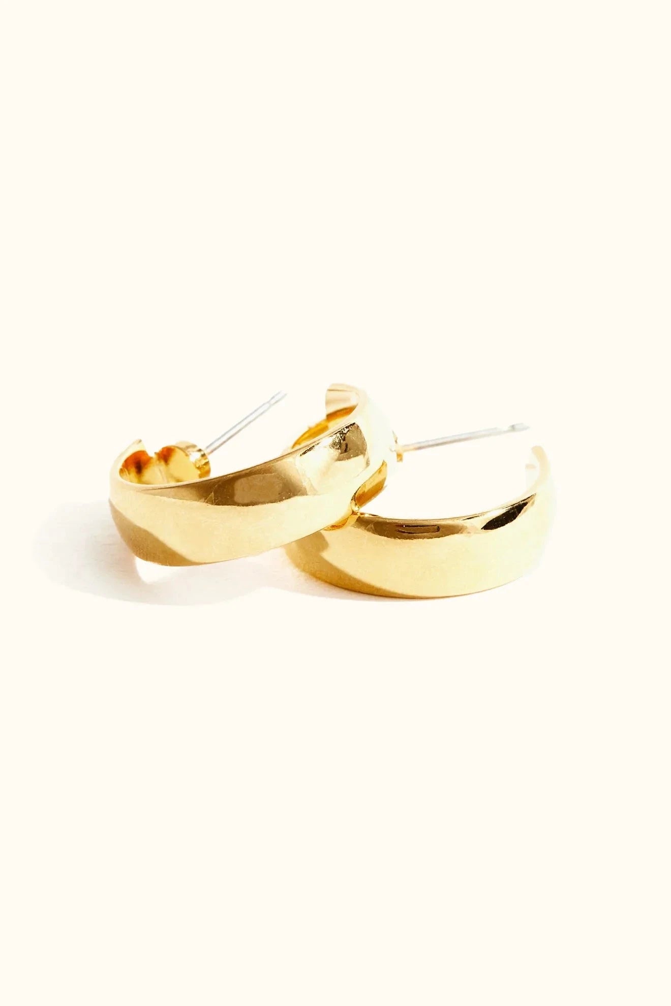 A pair of gold-plated brass hoop earrings with a shiny finish, displayed against a white background.