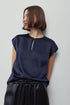 A woman wearing a navy blue short-sleeve top with a small gold-toned zipper detail at the neckline, paired with black satin-like pants, photographed against a plain light gray background.