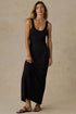 A woman modeling a black sleeveless maxi dress against a textured beige studio backdrop.