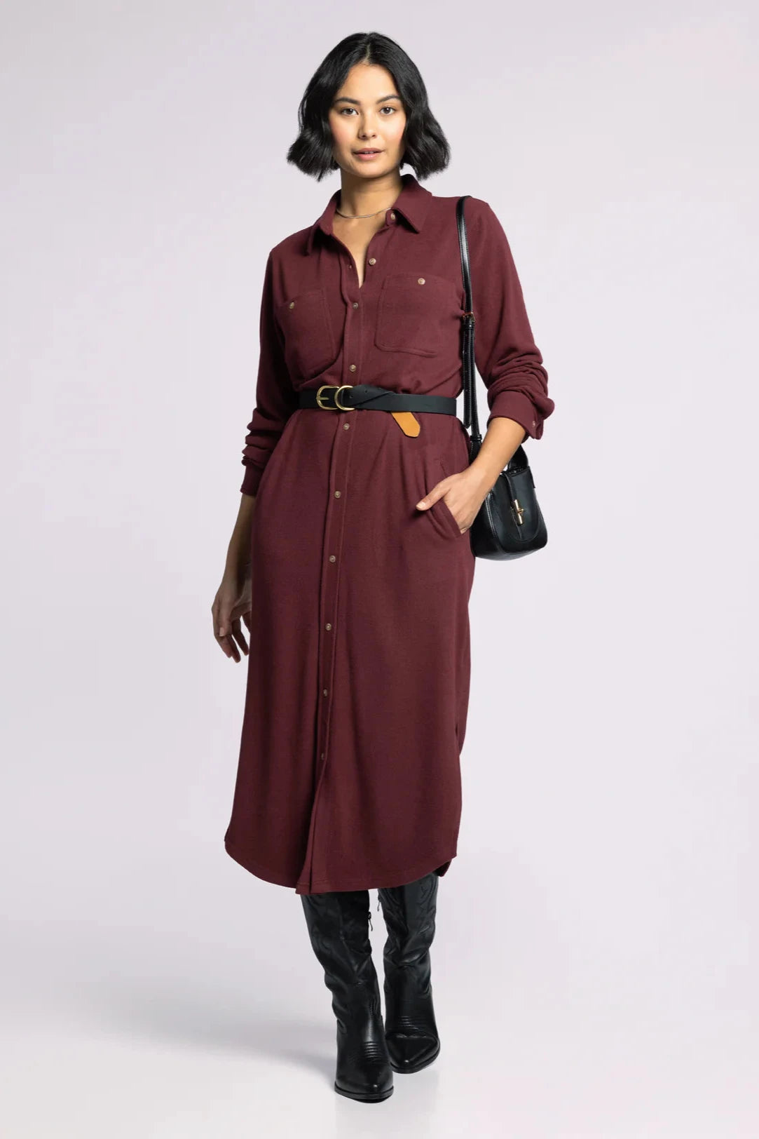 Woman wearing a burgundy dress with a black belt and bag on a white background