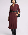 Woman wearing a burgundy dress with a black belt and bag on a white background