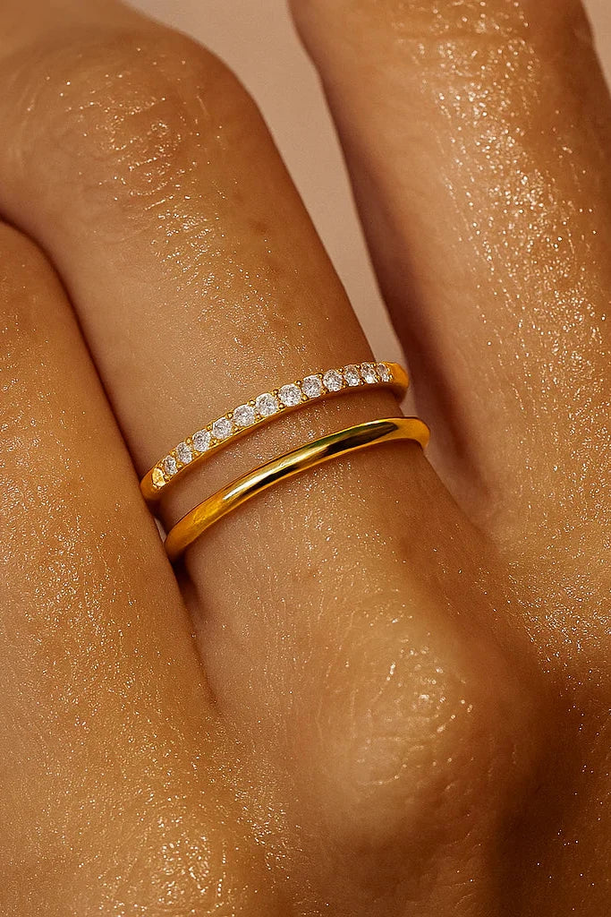 Close-up of a hand wearing two gold rings with diamond accents on a beige background