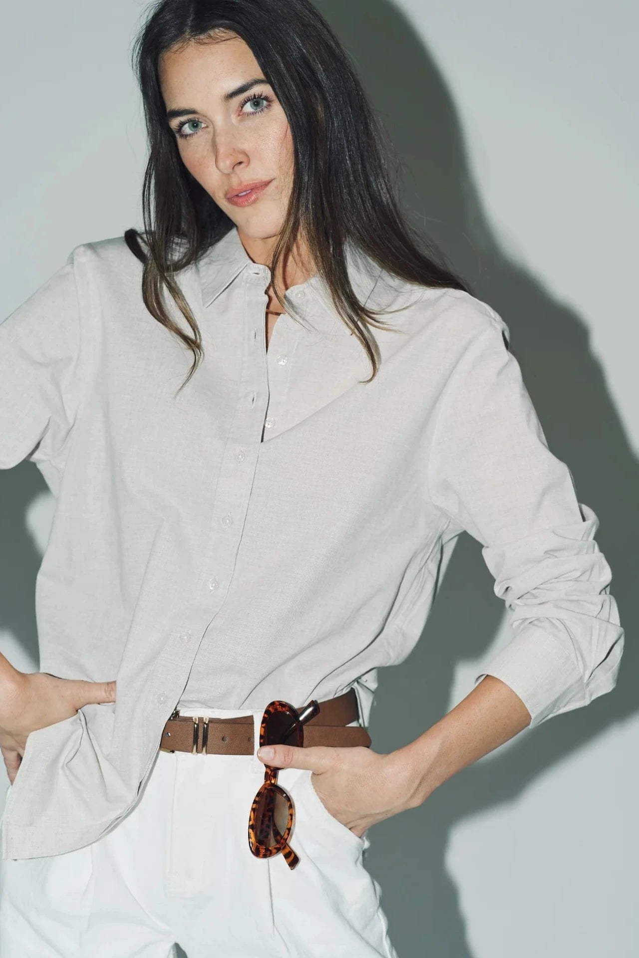 Woman wearing a light gray shirt and white pants against a plain background