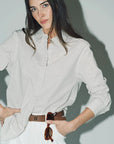 Woman wearing a light gray shirt and white pants against a plain background