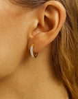 Close-up of an ear wearing a gold hoop earring with clear stones.