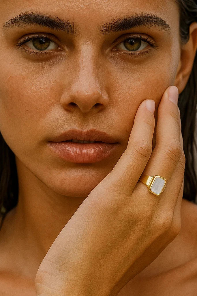 Woman with a gold ring on her finger touching her face outdoors