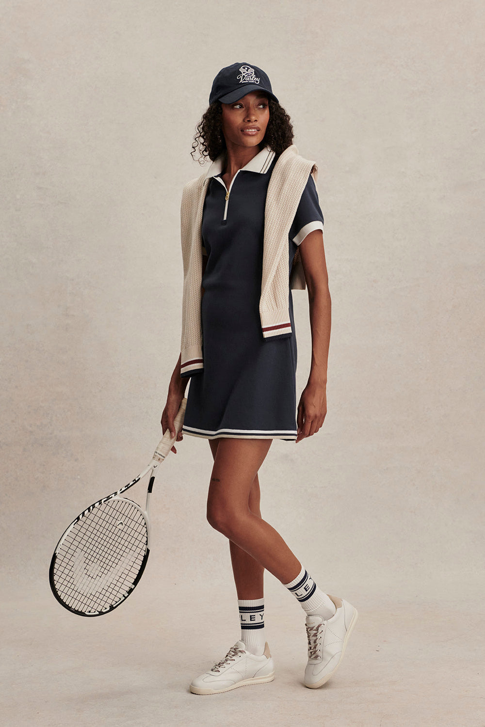 Woman in a navy and white tennis outfit holding a racket on a neutral background