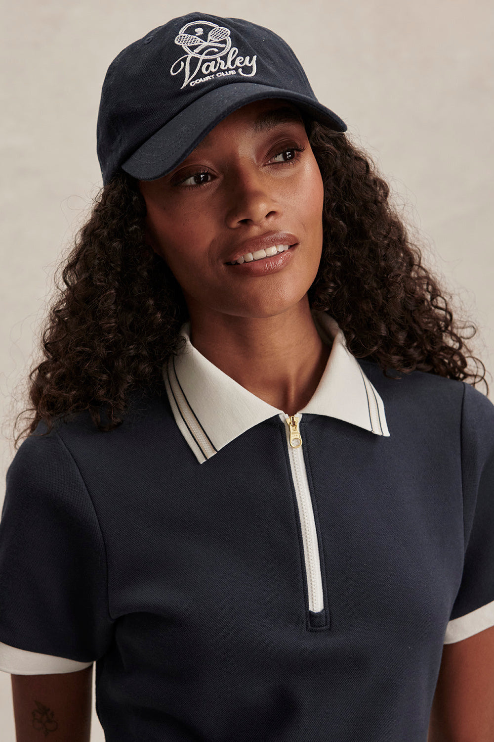 Woman wearing a navy cap and matching polo shirt with white accents on a neutral background