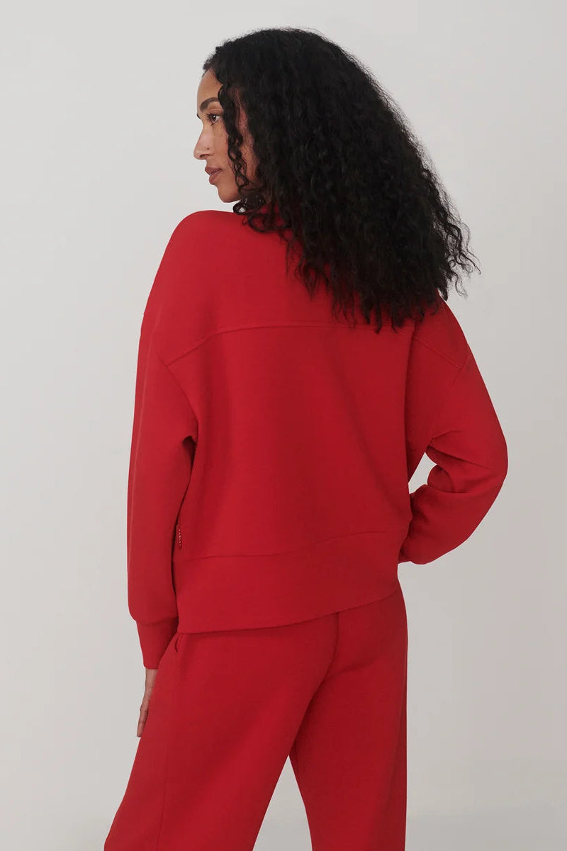 A model with long, curly black hair is shown from the back wearing a bright red cropped sweatshirt and matching red sweatpants against a plain light gray studio background.