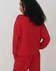 A model with long, curly black hair is shown from the back wearing a bright red cropped sweatshirt and matching red sweatpants against a plain light gray studio background.