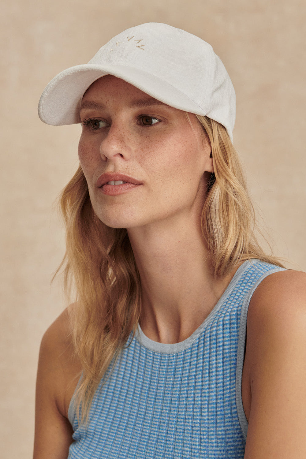 Woman wearing a white cap and blue tank top against a beige background