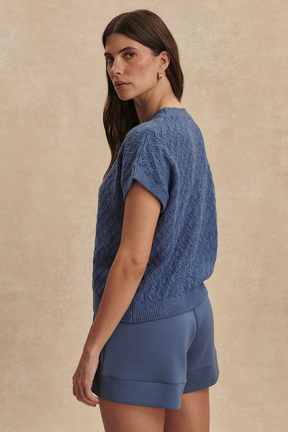 Woman wearing a blue knitted top and shorts on a beige background