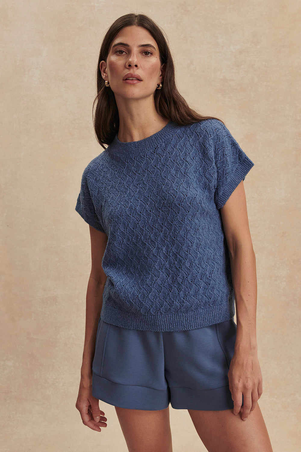 Woman wearing a blue knitted top and shorts against a beige background