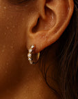 Close-up of an ear wearing a gold hoop earring with small pearls.