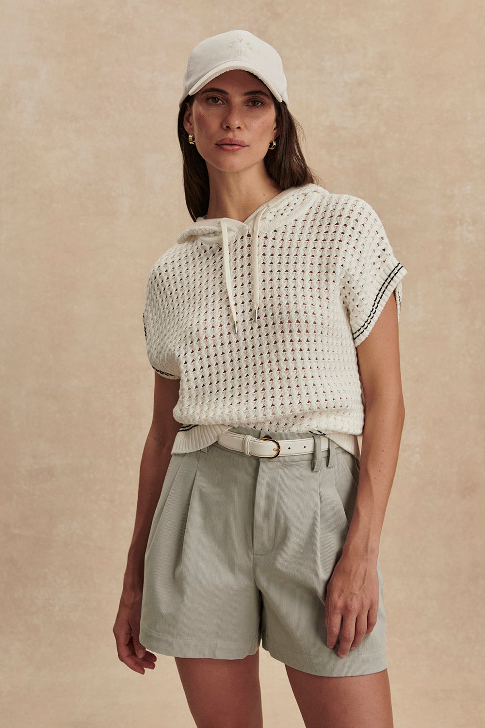 Woman wearing a white textured top and beige shorts against a beige background