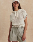 Woman wearing a white textured top and beige shorts against a beige background