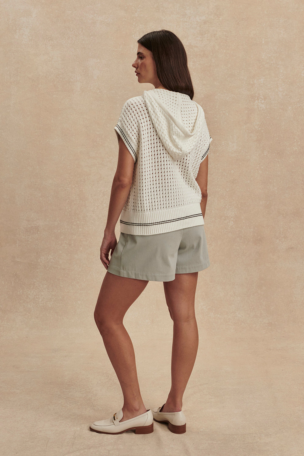 Woman wearing a light-colored knit top and shorts on a beige background