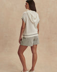 Woman wearing a light-colored knit top and shorts on a beige background