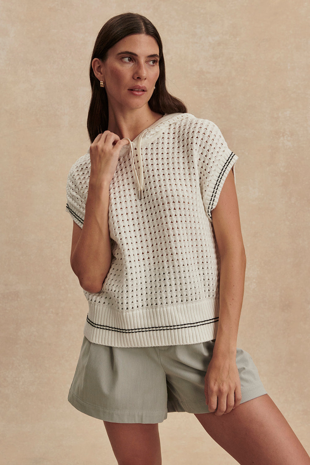 Woman wearing a white patterned top and beige shorts against a beige background