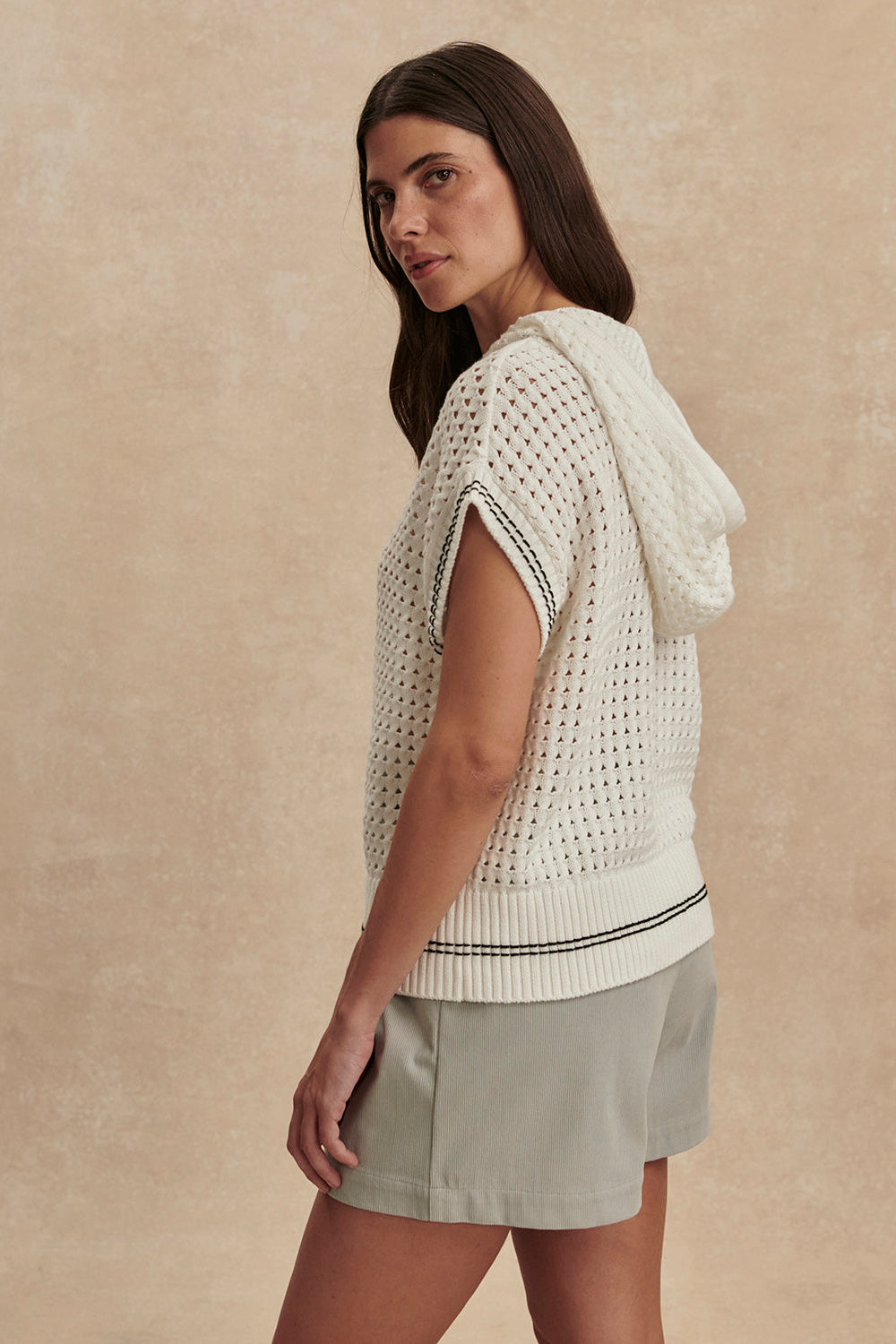 Woman wearing a white crochet top and light green shorts against a beige background