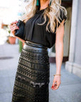 Woman wearing a black dress with intricate patterns and embellishments outdoors.