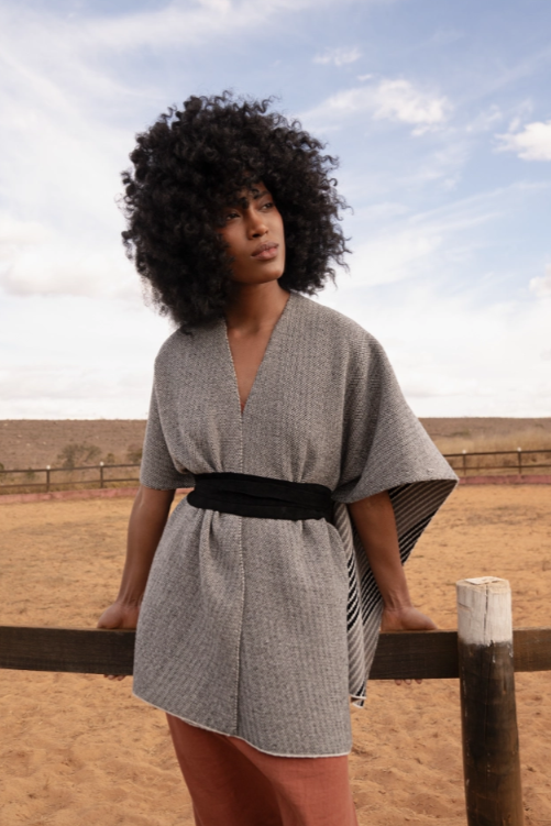 Woman wearing a gray dress with a black belt standing in a desert-like landscape.