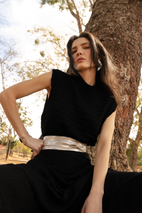 Woman in a black dress with a silver belt sitting against a tree