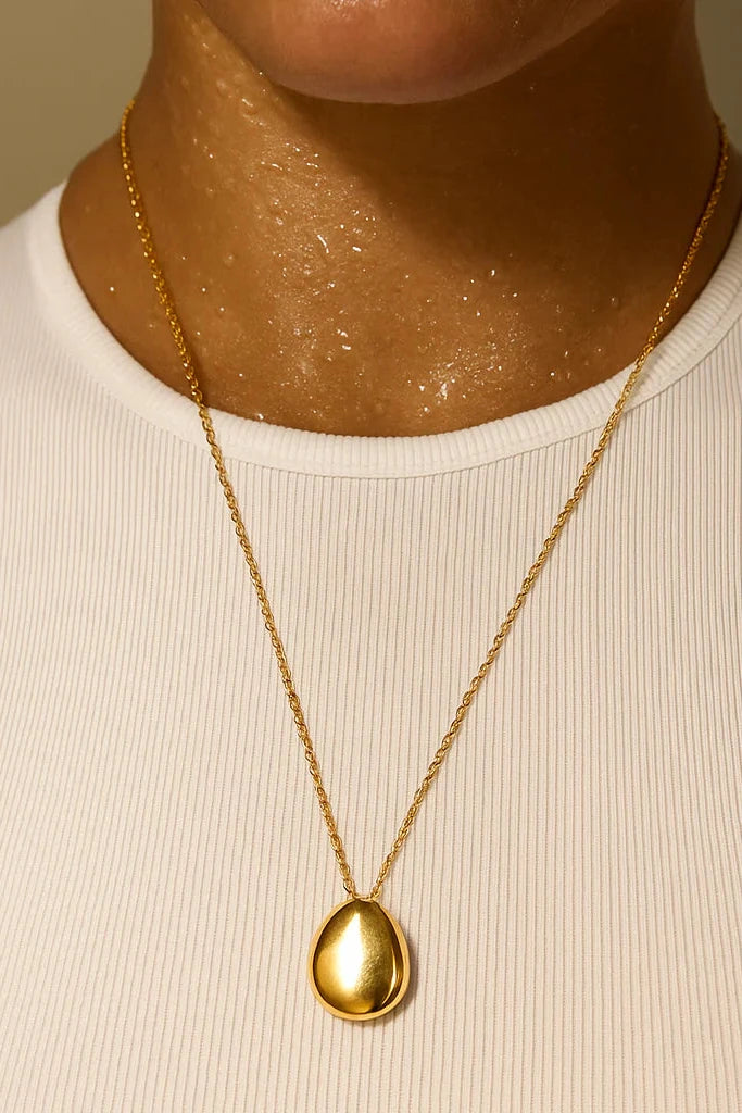 Gold necklace with a pendant worn by a person in a white tank top against a neutral background