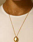 Gold necklace with a pendant worn by a person in a white tank top against a neutral background