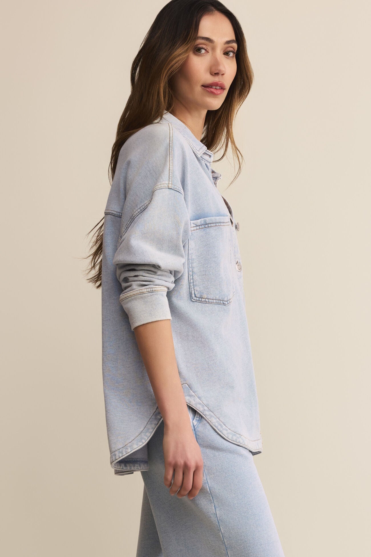 Woman wearing a light blue denim jacket and jeans on a beige background