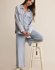 Woman sitting on a stool wearing a light blue denim outfit against a beige background