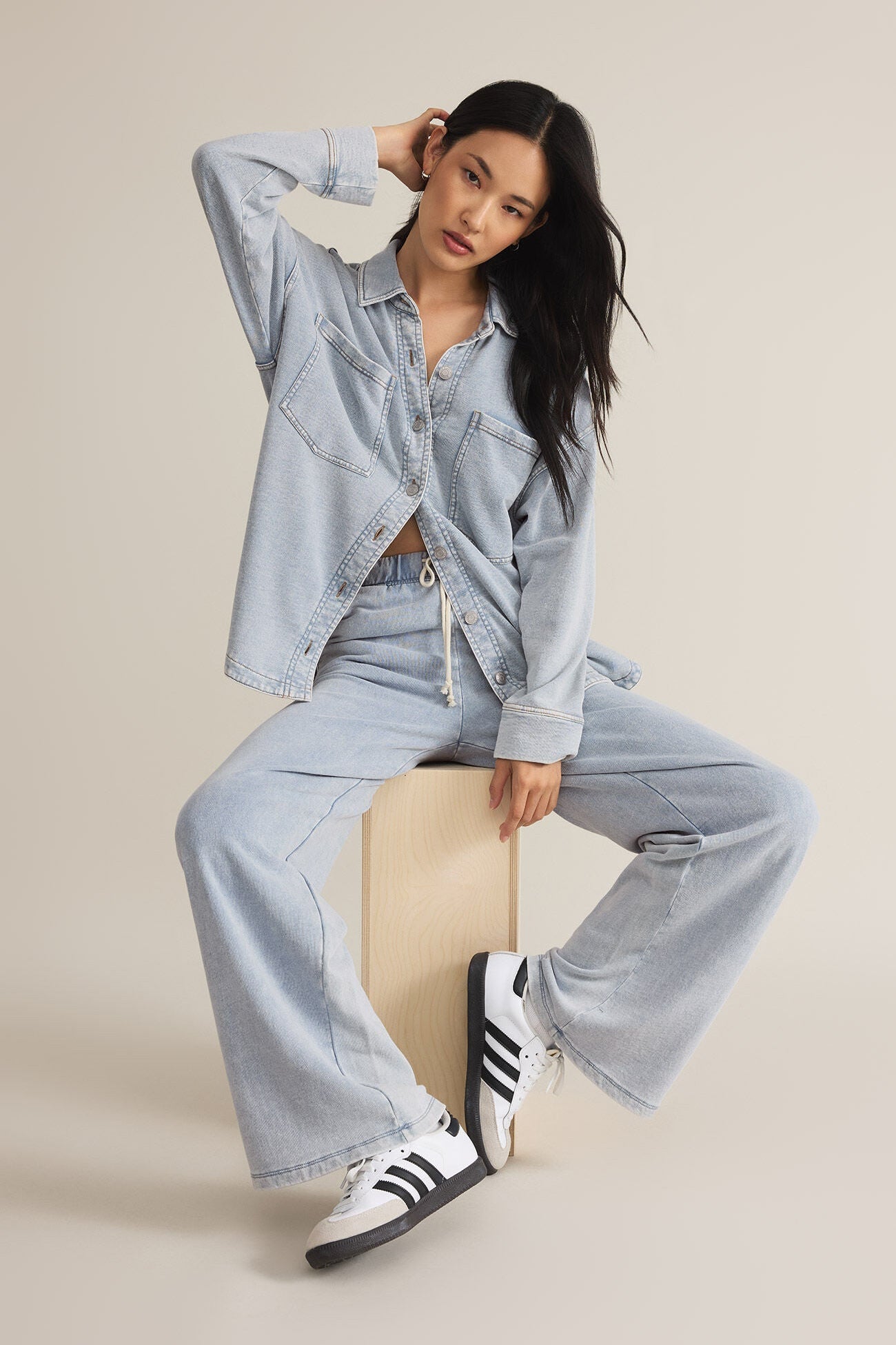 Woman wearing a light blue denim outfit with Adidas shoes on a beige background