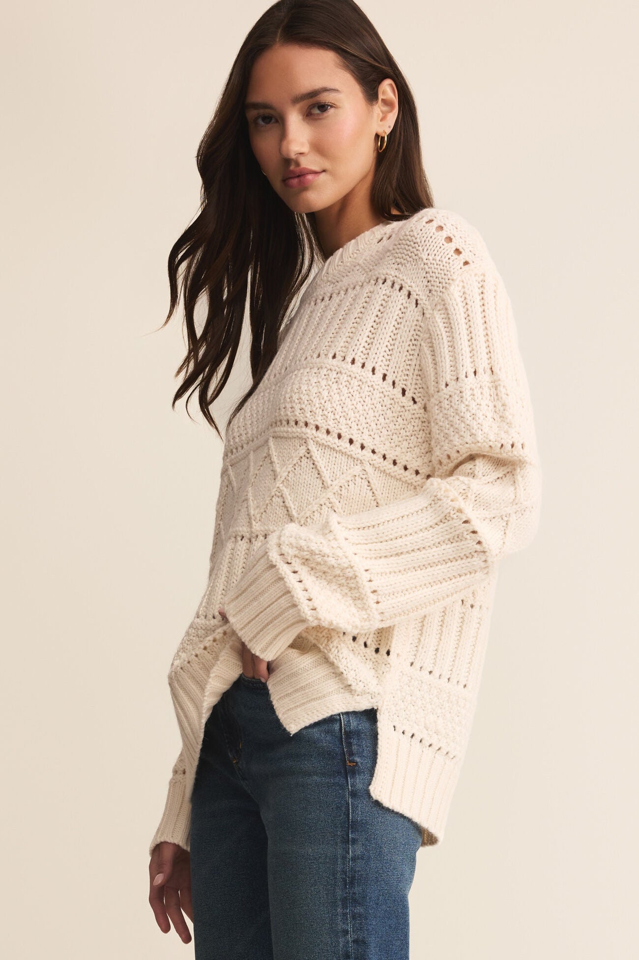Woman wearing a cream knitted sweater and blue jeans on a beige background