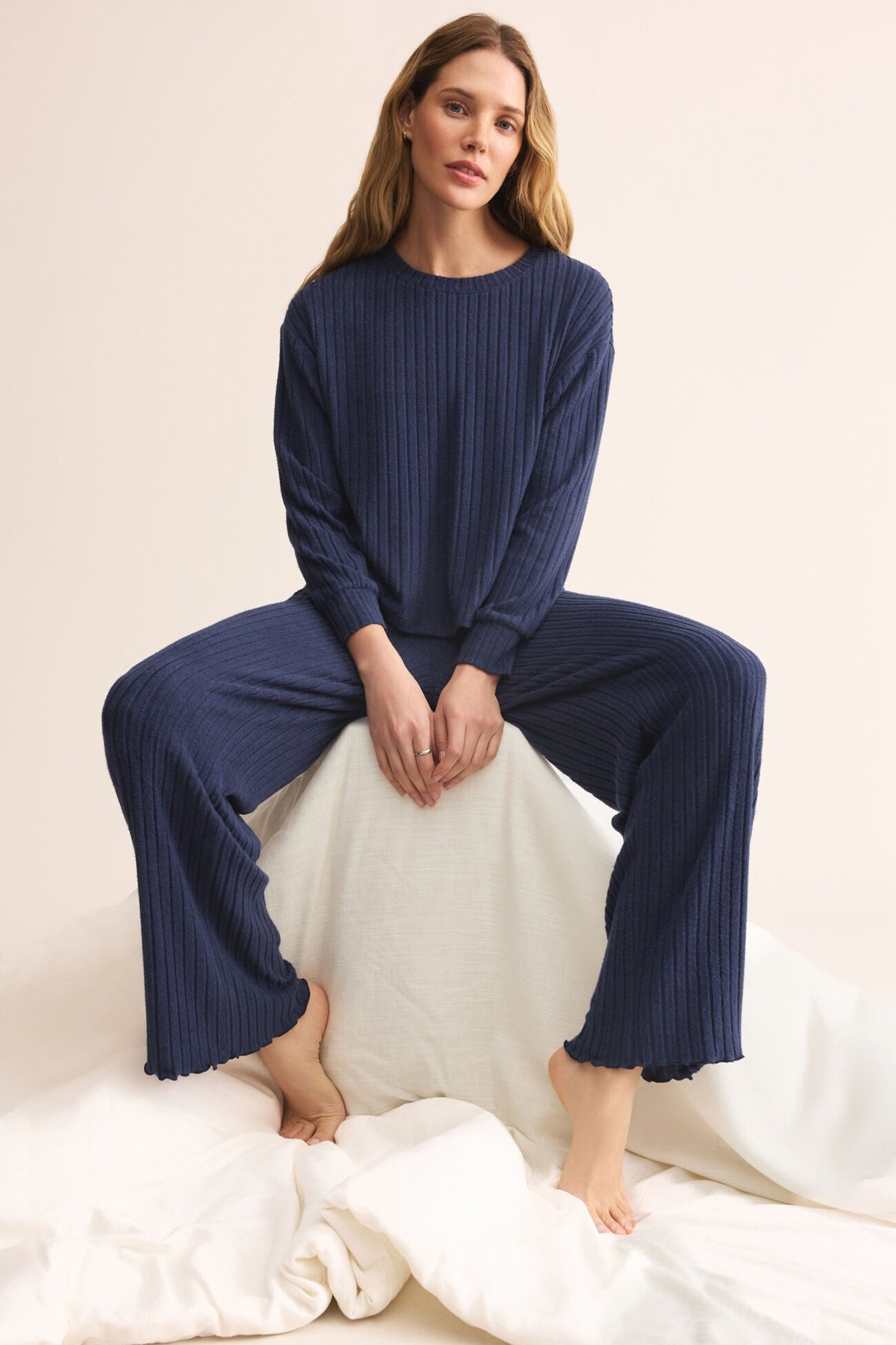 Woman wearing a navy ribbed pajama set sitting on a white surface.