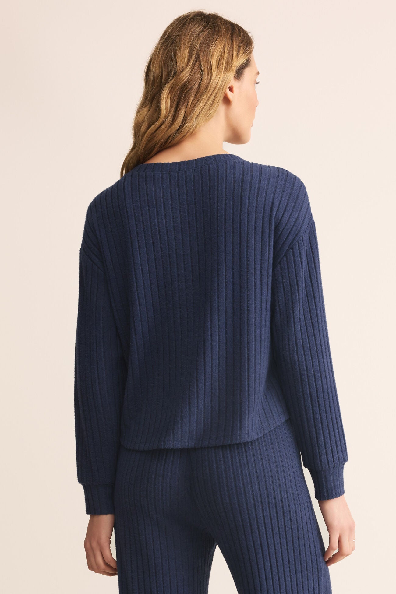 Person wearing a blue ribbed sweater and pants on a beige background