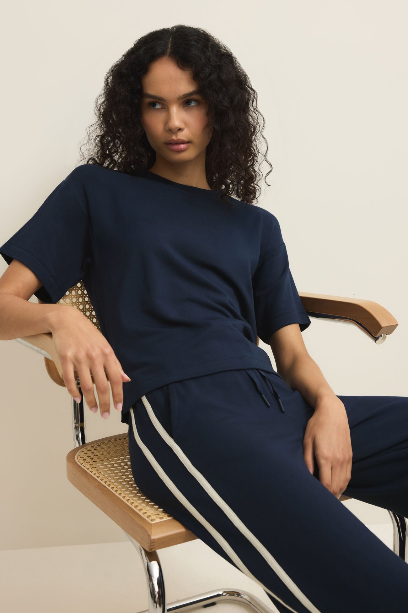 Woman wearing a navy blue outfit with white stripes sitting on a chair.