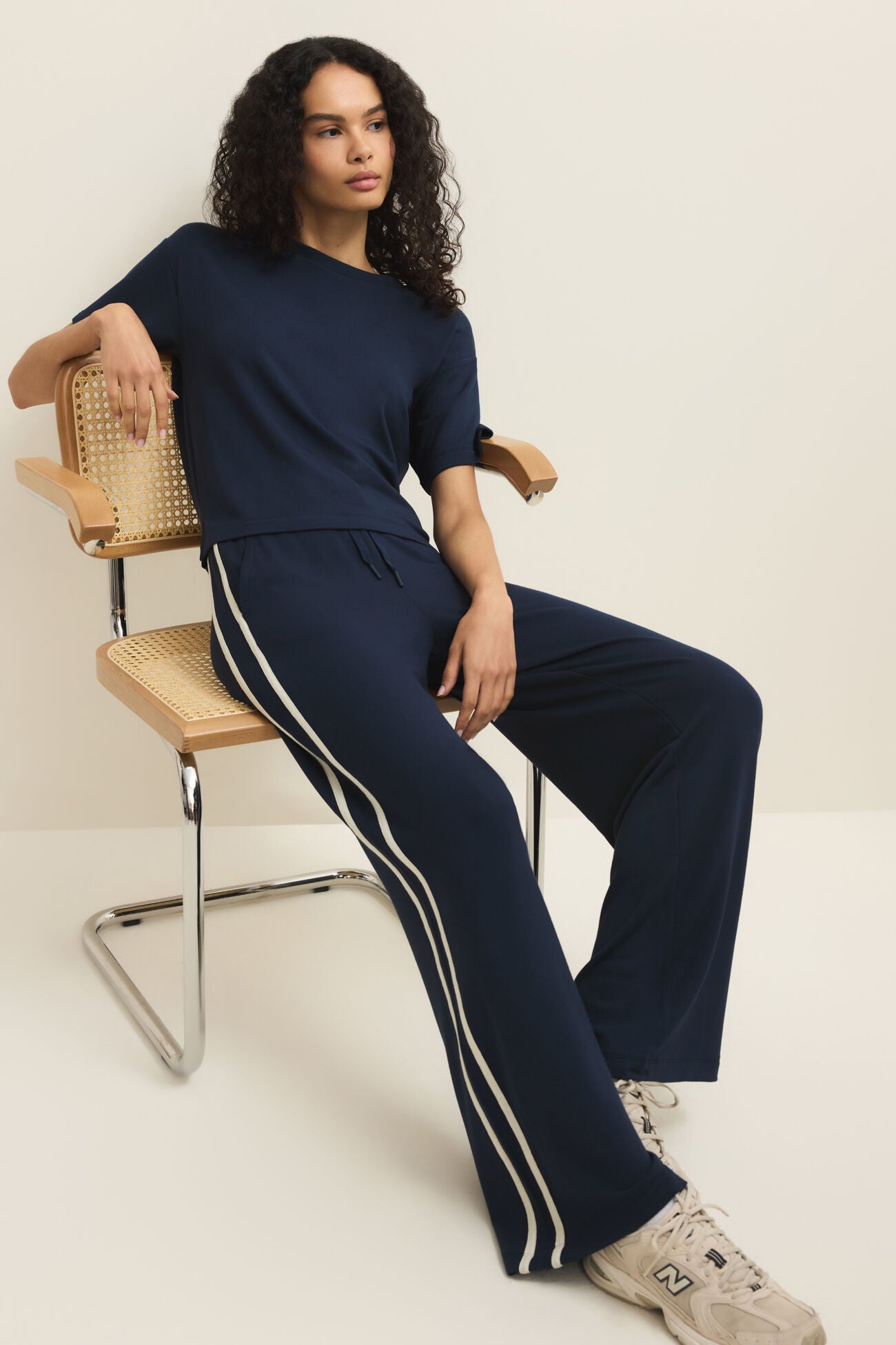 Woman sitting on a chair wearing a navy tracksuit with white stripes.