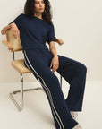 Woman sitting on a chair wearing a navy tracksuit with white stripes.