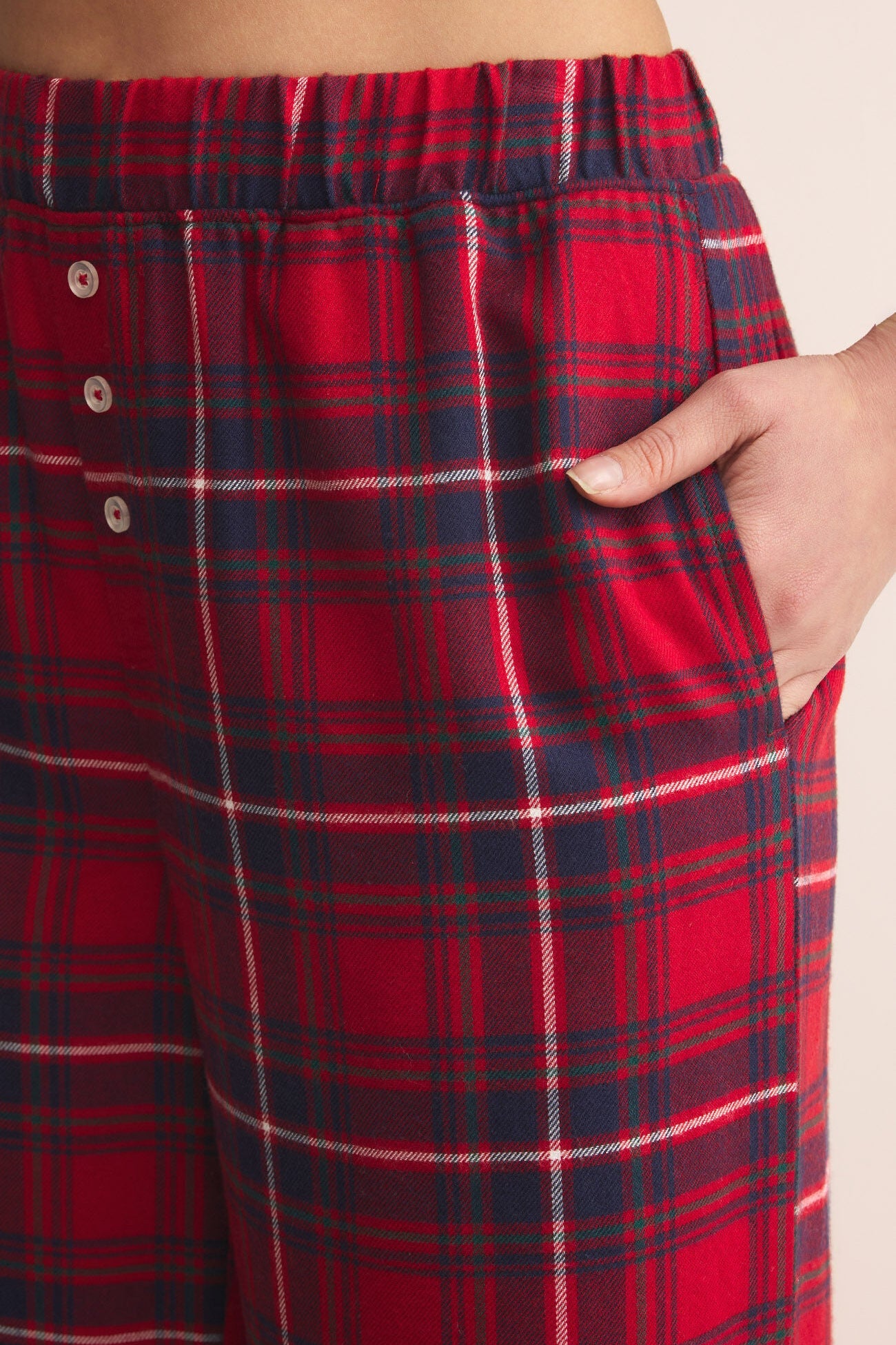 Red and blue plaid pajama pants with a hand in the pocket on a beige background