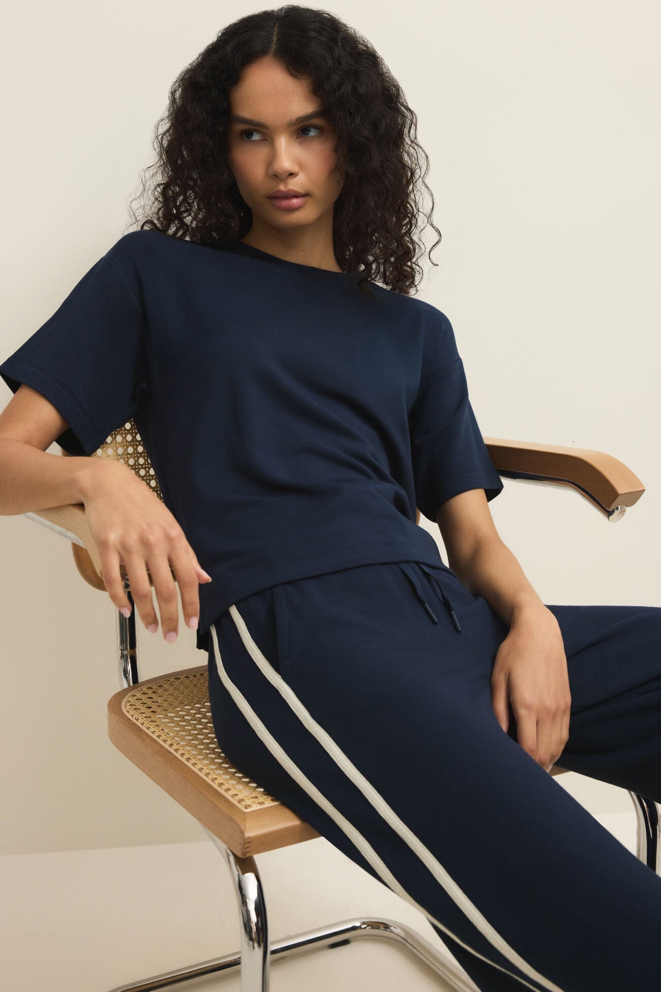 Woman wearing a navy blue outfit with white stripes sitting on a chair.