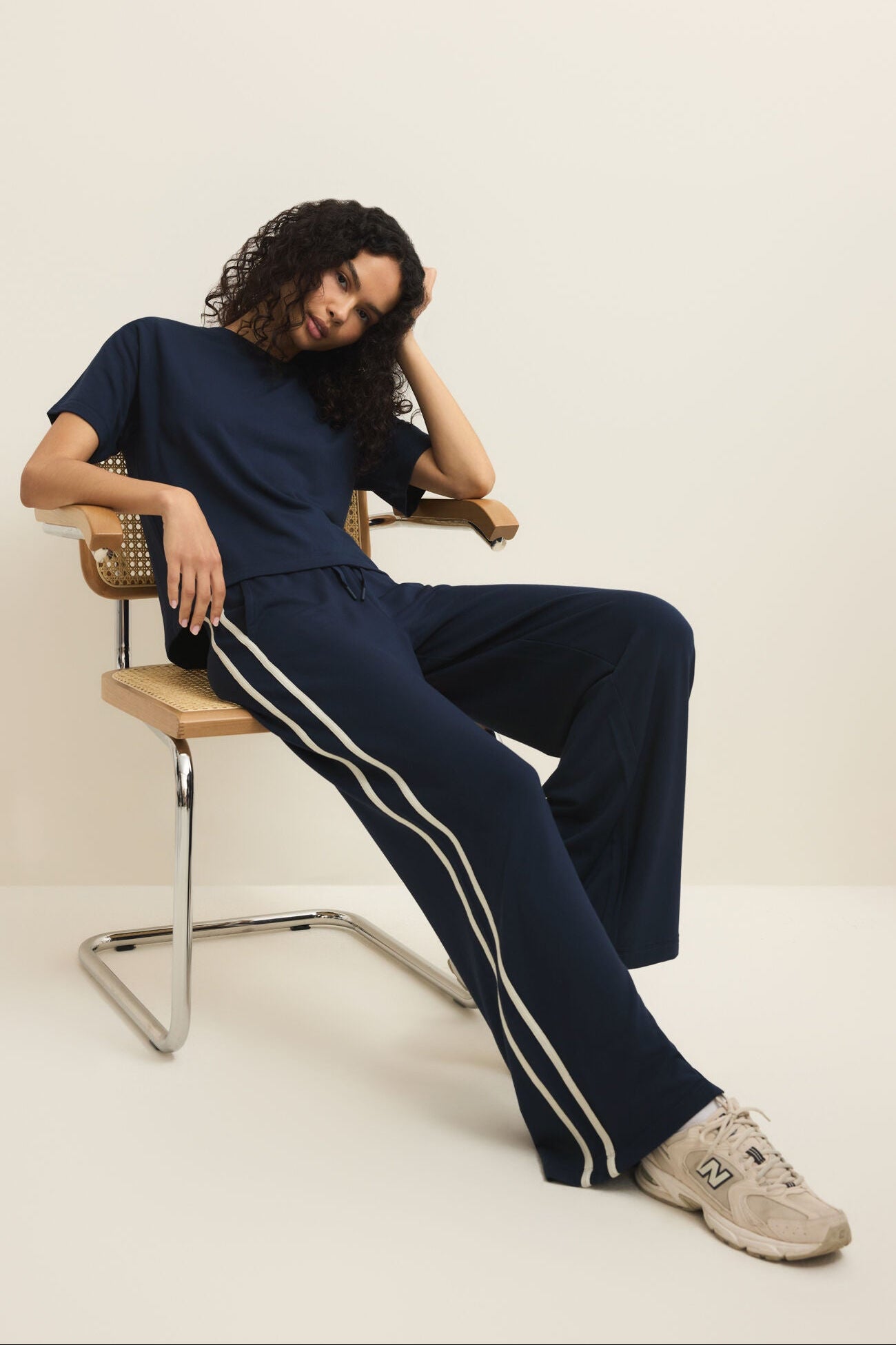 Person wearing a navy tracksuit with white stripes sitting on a chair against a plain background