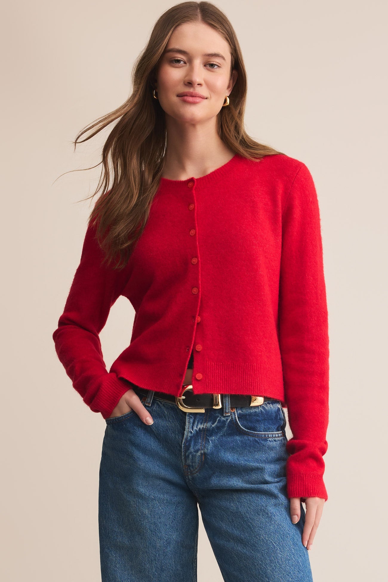 Woman wearing a red cardigan and blue jeans on a beige background