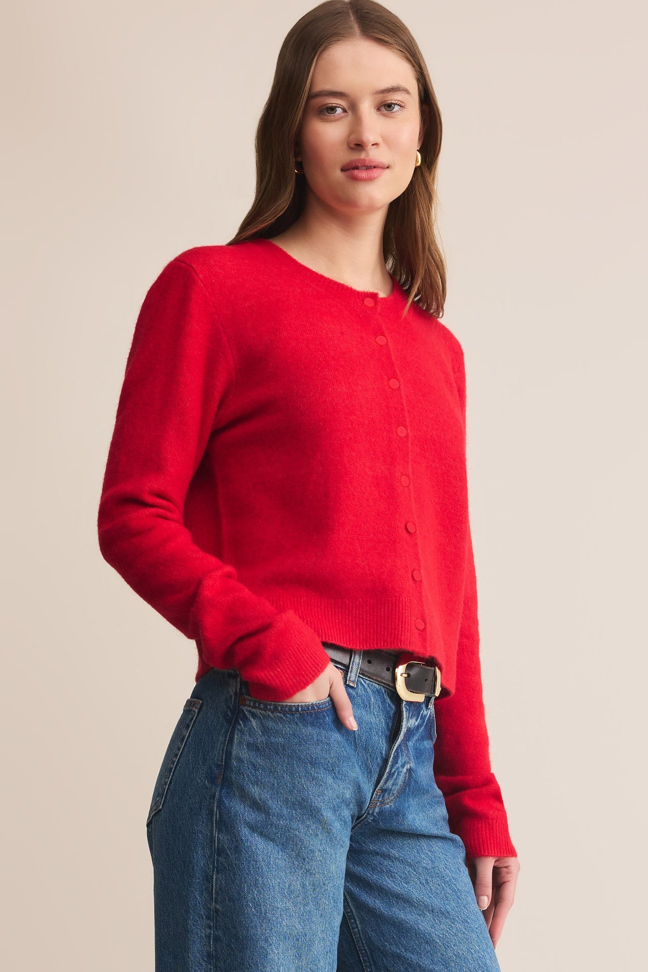 Woman wearing a red sweater and blue jeans against a beige background