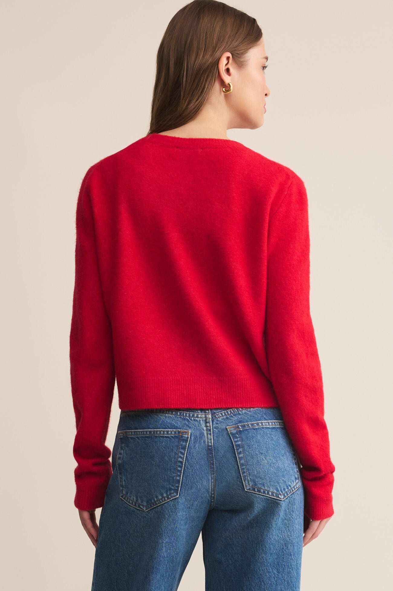 Person wearing a red sweater and blue jeans on a beige background