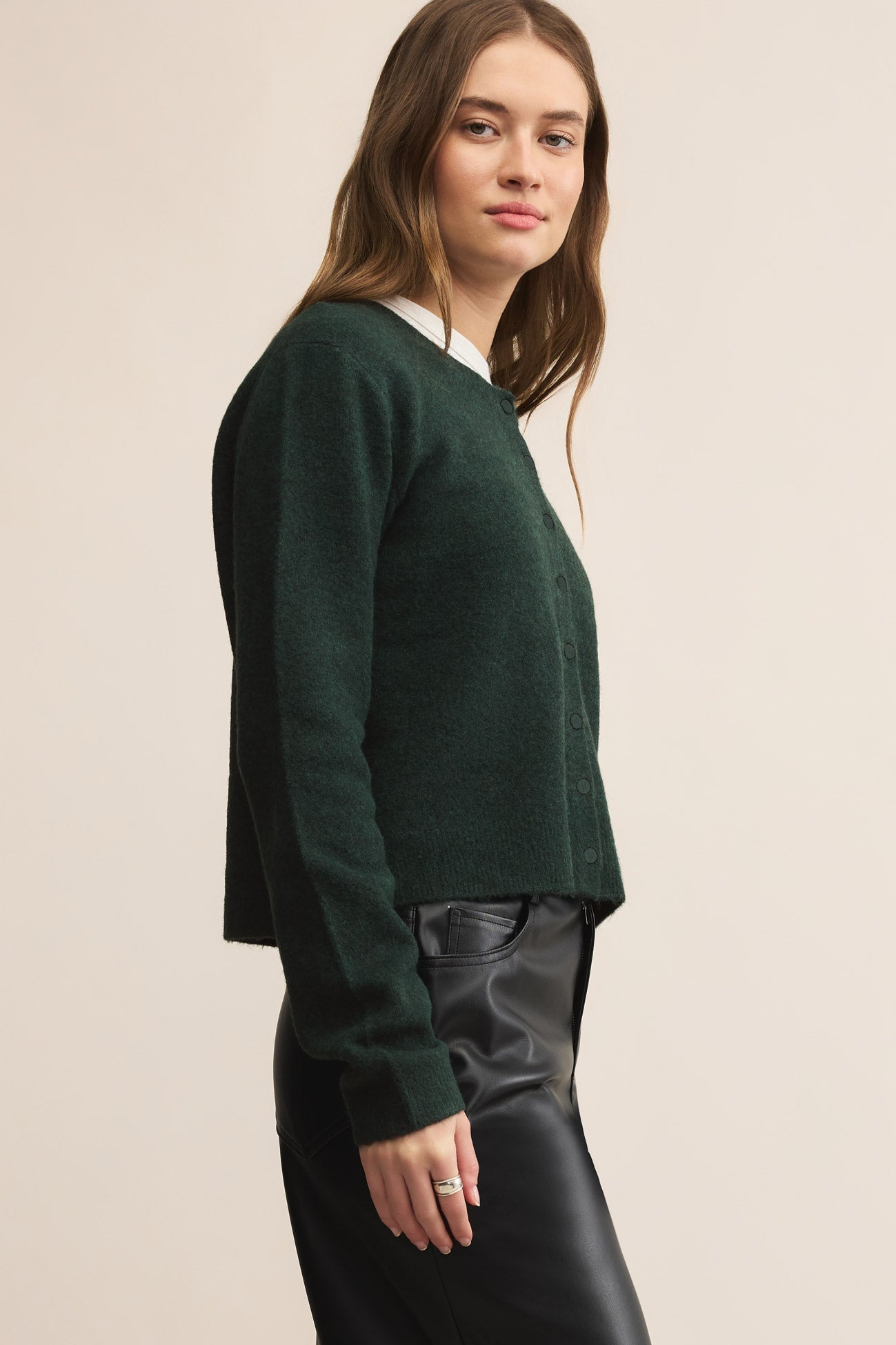 Woman wearing a green cardigan over a white shirt with black pants on a beige background