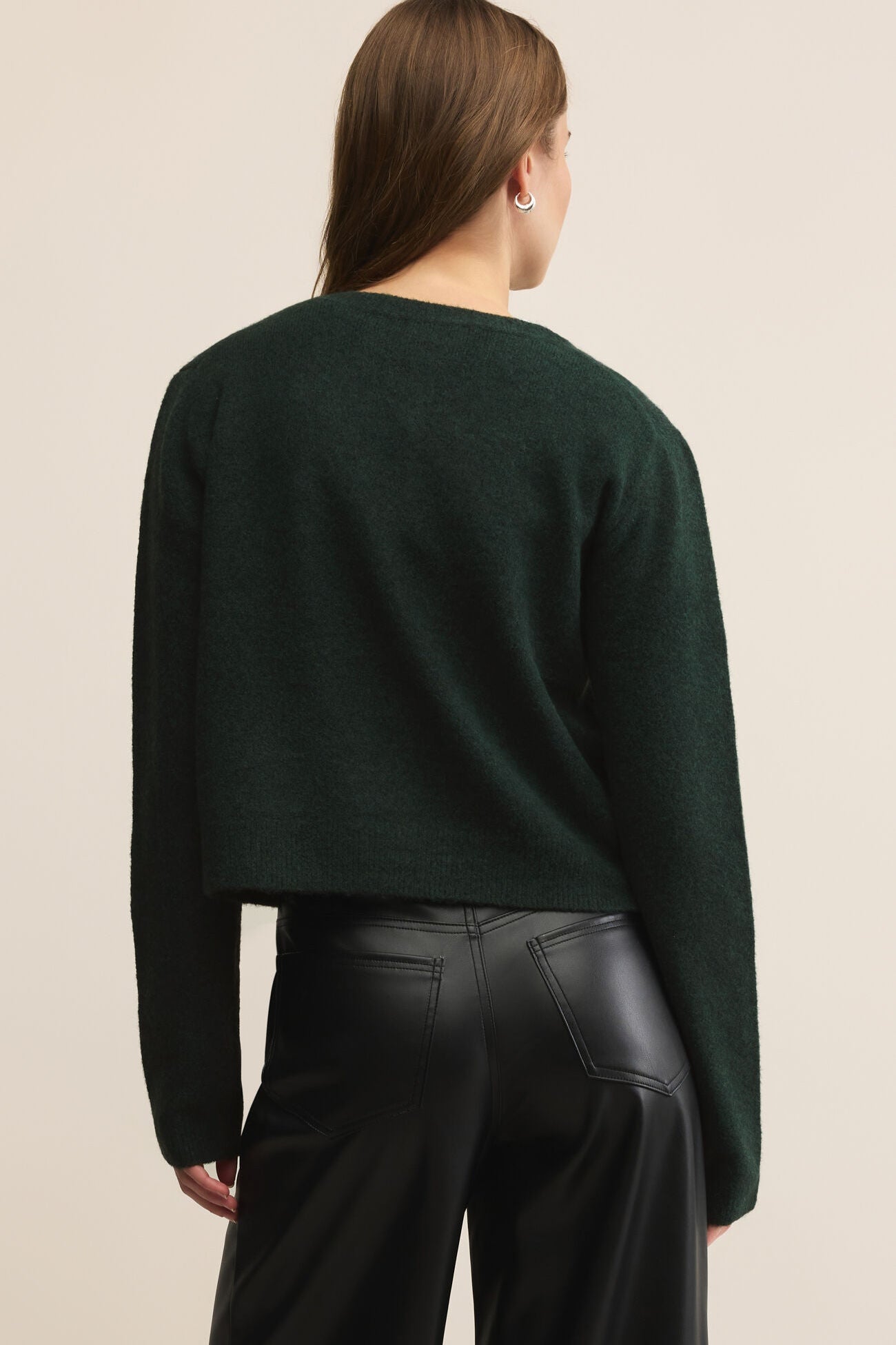Person wearing a dark green sweater and black pants on a beige background